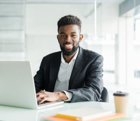 Portrait de beau jeune homme d'affaires noir africain travaillant sur ordinateur portable au bureau